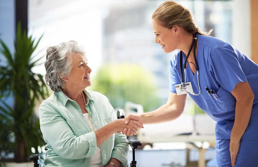 Older couple shares a meal in a bright assisted living apartment while a caregiver offers discreet support.